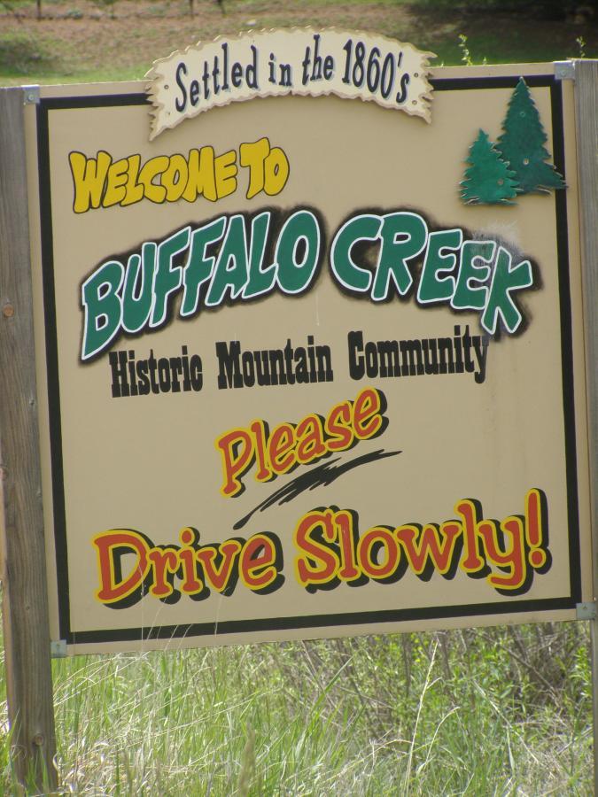 Sign welcoming visitors to Buffalo Creek, a historic mountain community settled in the 1860s, with an instruction to drive slowly. Buffalo Creek mountain bike trail.
