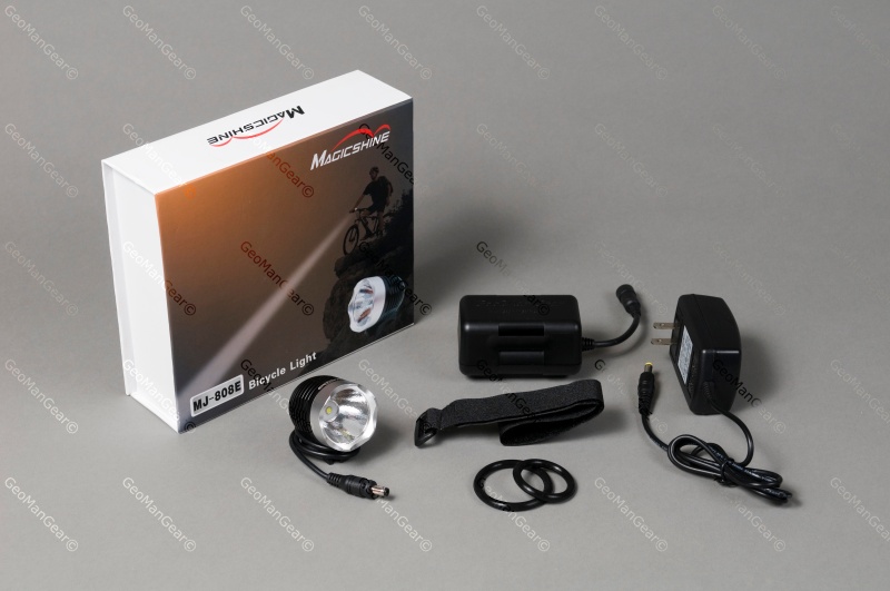 Alt text: A bicycle light set including a round LED light, a battery pack, a charger, a mounting strap, and additional rubber rings, arranged next to its packaging labeled "MJ-808E Bicycle Light."