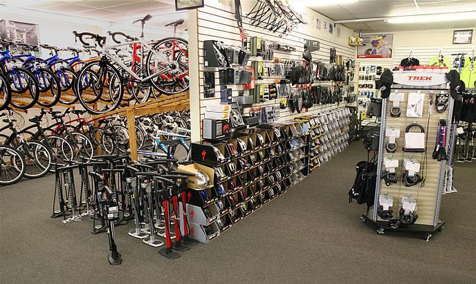 Alt tag: "Interior of a bicycle shop featuring various bicycles on display, shelves stocked with cycling accessories, helmets, and repair tools, along with a standing display for a popular bike brand."