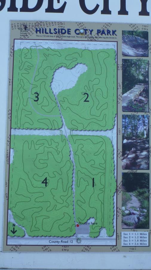 Map of Hillside City Park, showing a 2.75-mile loop trail divided into four sections, with marked distances for each section. The map indicates the location of the viewer with a red dot labeled "You are here," and includes photographs of park features. The park is situated near County Road 12. Hillside Park mountain bike trail.
