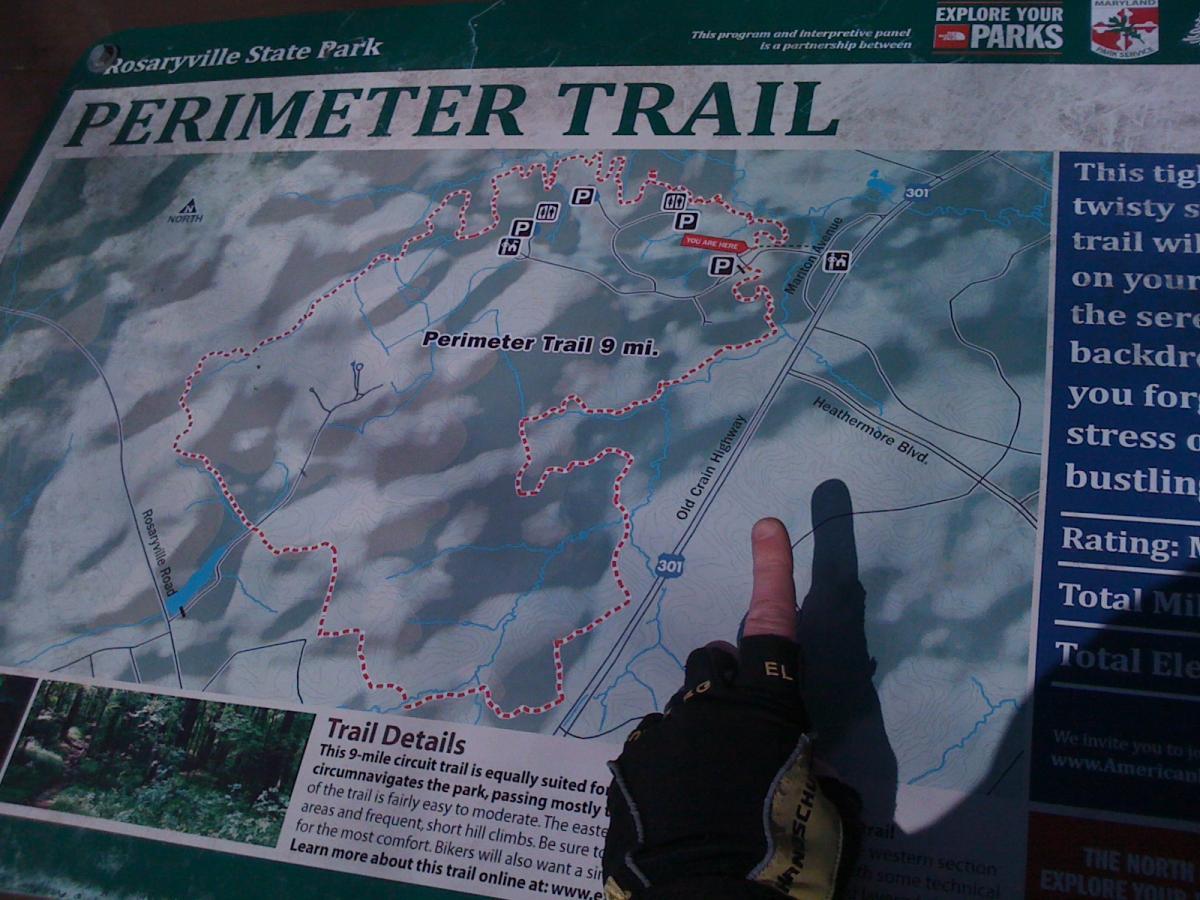 Map of the Perimeter Trail at Rosaryville State Park, featuring a 9-mile circuit trail depicted with a dotted red line. The map indicates parking areas and the current location marked as "YOU ARE HERE." Included are trail details highlighting the terrain and length. Rosaryville State Park mountain bike trail.