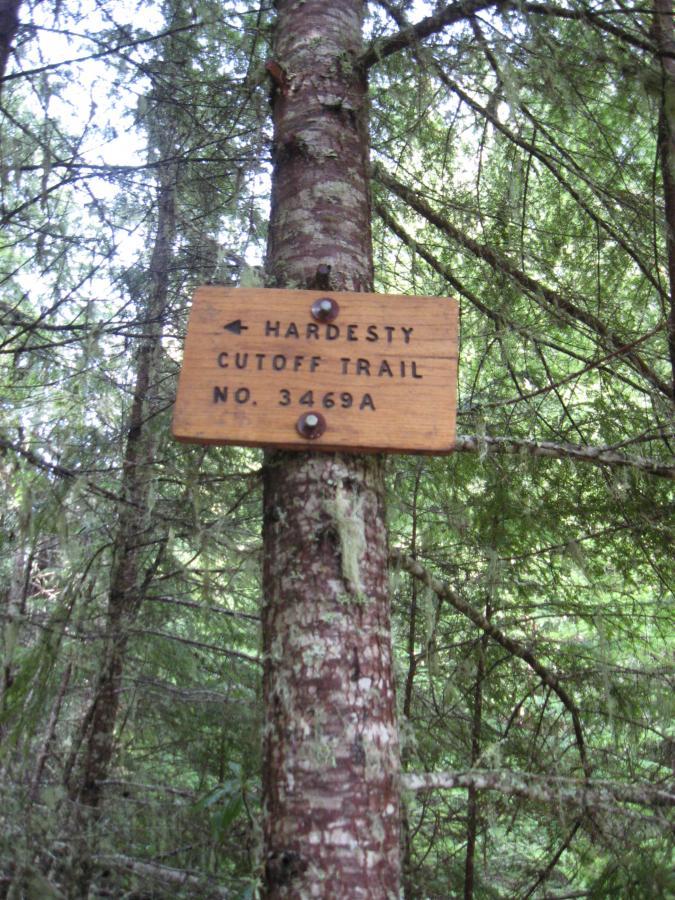 A wooden trail sign attached to a tree in a dense forest, indicating "Hardesty Cutoff Trail" with a trail number "No. 3469A." The sign is weathered and surrounded by greenery, including various trees and foliage. Eula Ridge mountain bike trail.