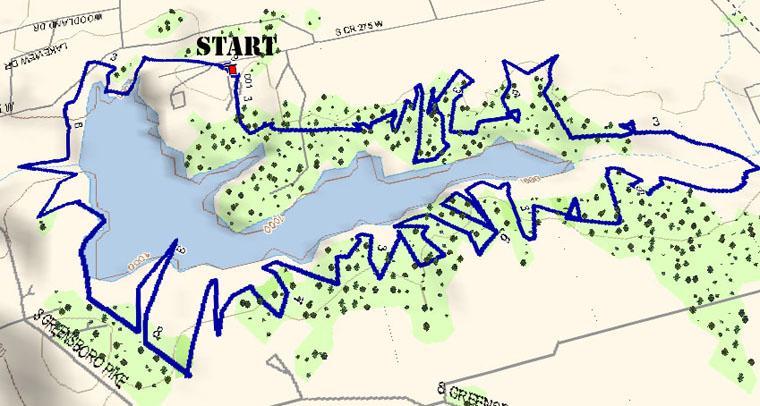 A detailed map showing a blue trail route around a lake, with marked points including a "START" location. The surrounding area features green spaces with scattered trees, indicating a natural landscape. The route has a winding pattern, suggesting it may be intended for hiking, biking, or walking activities. Westwood Trails mountain bike trail.
