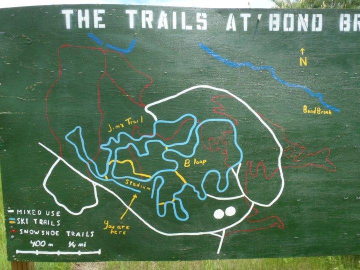 Map of the trails at Bond Brook, featuring paths for mixed use, skiing, and snowshoeing. Key landmarks include Jim's Trail and the B Loop. The map indicates the user's current location with a marker and includes a directional compass. Bond Brook Trails mountain bike trail.