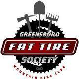 Logo of the Greensboro Fat Tire Society, featuring a stylized bicycle gear with a shovel, a pickaxe, and a rake crossed behind it. The text "GREENSBORO" is displayed at the top, and "FAT TIRE SOCIETY" is prominently featured in the center, with "MOUNTAIN BIKE CLUB" at the bottom. The overall color scheme includes black, red, and white.