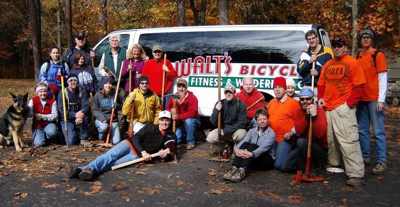 A large group of people poses outdoors in front of a van with the logo "Walt