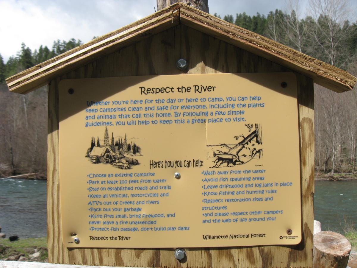 A wooden sign titled "Respect the River" with guidelines for campers. The sign advises on proper camping practices, such as choosing existing campsites, staying 100 feet away from water, and protecting wildlife. It features an illustration related to the message and is located near a river in the Willamette National Forest. Middle Fork Trail mountain bike trail.