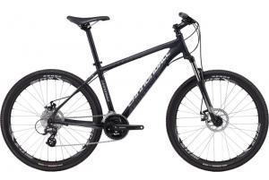 Cannondale Trail 6: Mountain bike with a black frame, front suspension, and disc brakes. It features wide tires designed for off-road terrain and a gear shifter on the handlebars.