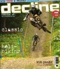 * Decline: Cover of the magazine "Decline" featuring a mountain biker performing a jump on a dirt path surrounded by trees. The cover includes text highlighting topics like "classic" and "heli-biking."