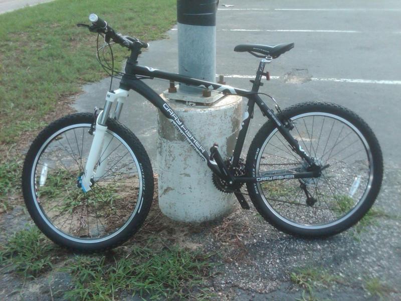 Gary Fisher Wahoo: A black and white mountain bike leaning against a concrete post in a grassy area, with a paved parking lot visible in the background.