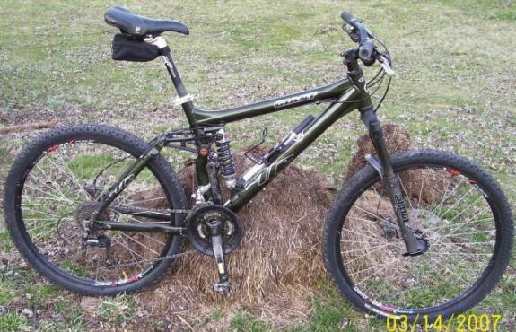 Giant AC: A black mountain bike with front suspension, positioned on a grassy area next to some hay or straw. The bike features large tires, a visible rear shock absorber, and a small pouch attached to the seat. The image is dated March 14, 2007.