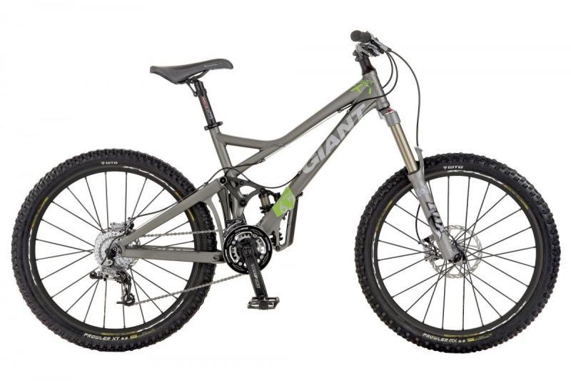Giant Reign X1: A gray mountain bike with green accents, featuring broad tires, a dual suspension system, and a modern frame design. The bike is positioned upright against a plain background.