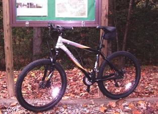 Giant Rincon: A mountain bike parked on a trail surrounded by autumn leaves, with a wooden information board in the background.