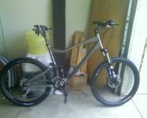 Giant Trance X1: A mountain bike with a gray frame, front suspension, and thick tires, positioned in a garage setting with various items in the background.