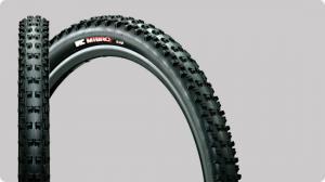 IRC Mibro: A mountain bike tire displayed against a gray background, featuring a knobby tread pattern for enhanced grip and traction. The tire is shown from the side and at an angle, highlighting its robust design.