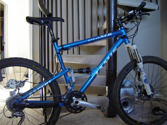Jamis Dakar XCR Expert: A blue mountain bike with a sturdy frame, featuring knobby tires, front suspension, and a visible drivetrain, positioned near a staircase in an indoor setting.