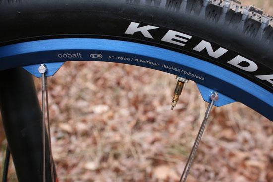 Kenda Tinker Juarez Dred Tread Tires: Close-up view of a bicycle wheel, featuring a blue rim labeled "cobalt" and a Kenda tire. The image shows the rim