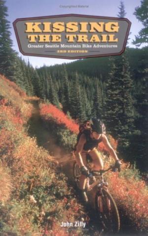 * Kissing the Trail: Greater Seattle Mountain Bike Adventures: Book cover of "Kissing the Trail: Greater Seattle Mountain Bike Adventures, 3rd Edition" by John Zilly. The cover features a mountain biker riding through a wooded trail with autumn foliage in vibrant colors.