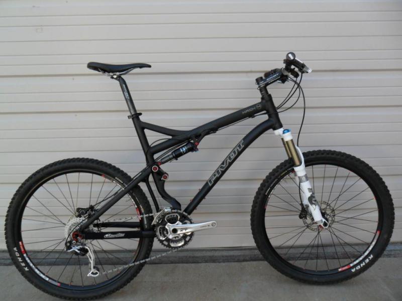 Pivot Mach 4: Mountain bike with a black frame, front suspension, and knobby tires, positioned against a white garage door.