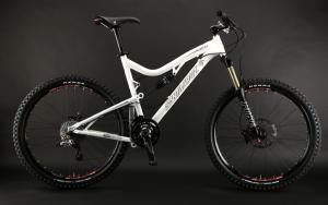Santa Cruz Blur LT2: A white mountain bike with front suspension, a black saddle, and knobby tires, displayed against a dark background.