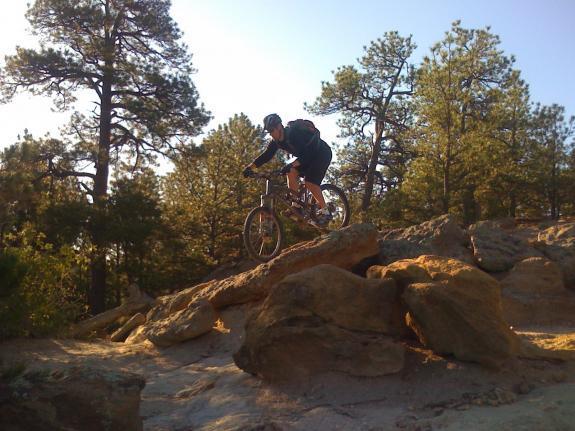 Santa Cruz Nomad: A mountain biker navigating rocky terrain in a forested area, with sunlight filtering through the trees.