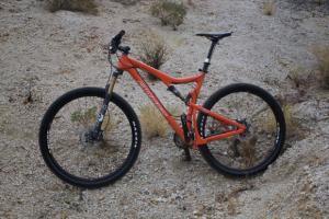 Santa Cruz Tallboy: A vibrant orange mountain bike positioned on a rocky, sandy terrain, surrounded by sparse vegetation.