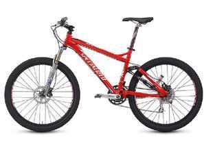 Specialized Epic Expert: A bright red mountain bike with a sleek frame, front suspension, and wide tires, positioned on a white background. The bike features disc brakes and a chain drive, highlighting its suitability for rugged terrains.