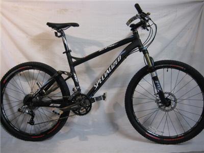 Specialized Epic: Alt text: A black Specialized mountain bike with a glossy finish, featuring a dual suspension system and thick tires. It is positioned against a plain white background, highlighting its sleek design and sturdy components.