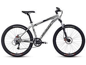 Specialized Rockhopper Comp Disc: A silver mountain bike with wide tires, front suspension, and a sleek frame, designed for off-road cycling.