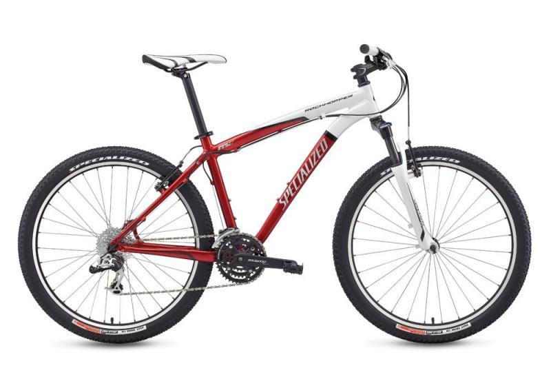 Specialized Rockhopper: A red and white Specialized mountain bike with a lightweight frame, dual suspension, and knobby tires designed for off-road riding. The bike features a sleek design with a prominent brand name on the frame and is positioned against a neutral background.