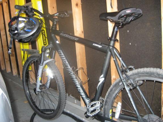 Specialized Rockhopper: A black mountain bike with a helmet resting on the handlebars, positioned in a garage setting with wooden walls and tools in the background.