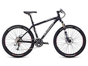 Specialized Stumpjumper Comp: A black mountain bike with a sleek design, featuring a sturdy frame, disc brakes, and thick tires designed for off-road riding. The bike is equipped with a front suspension fork and a gear shifter, highlighting its performance capabilities.
