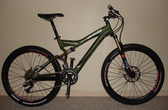 Specialized Stumpjumper Comp: A green mountain bike with disc brakes, featuring a lightweight frame and thick tires, positioned against a neutral-colored wall.