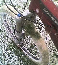 Specialized Stumpjumper Comp: A close-up image of the front wheel of a bicycle partially covered in snow, showing details of the bike's frame and tires against a snowy ground.