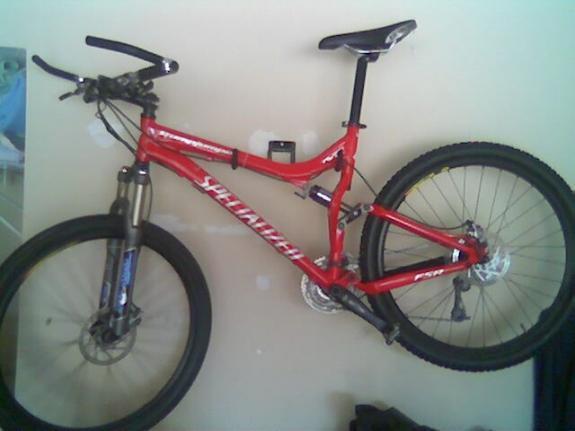 Specialized Stumpjumper FSR Expert: A red mountain bike mounted on a wall, featuring a front suspension fork and thick tires, with visible gear shifters and brake components.