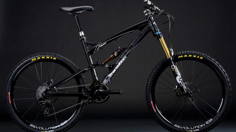 Transition Covert: A black mountain bike with a sleek design, featuring a dual suspension system, prominent front forks, and stylish Maxxis tires. The bike is positioned against a dark background, highlighting its modern frame and components.