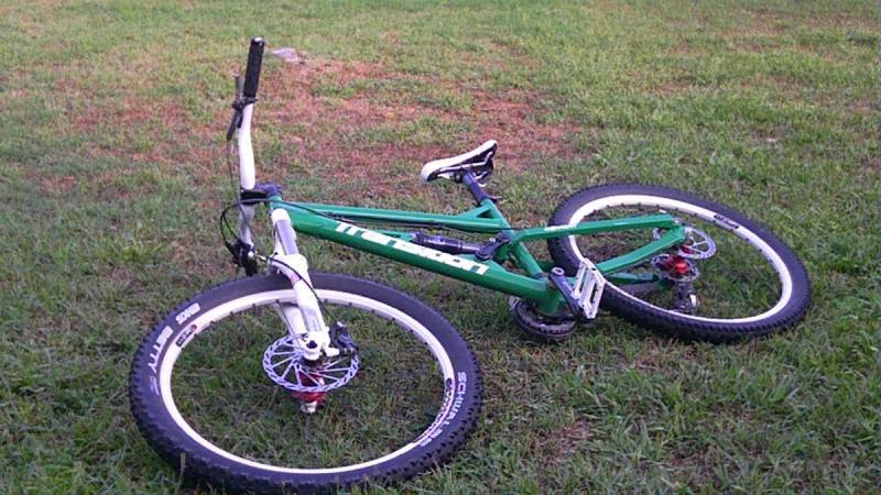 Transition Covert: A green mountain bike lying on its side on grassy ground, with both wheels visible and the handlebars turned to one side.