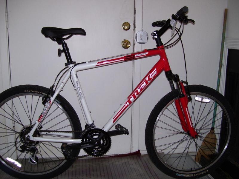 Trek 3700: A red and white Trek mountain bike leaning against a wall, showcasing its front tire and handlebars, with a closed door and floor visible in the background.