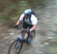 Trek 4300: A mountain biker riding down a rocky trail, captured in motion with a blurred background, suggesting speed and adventure. The rider is wearing a helmet and backpack, dressed in a white shirt and shorts.