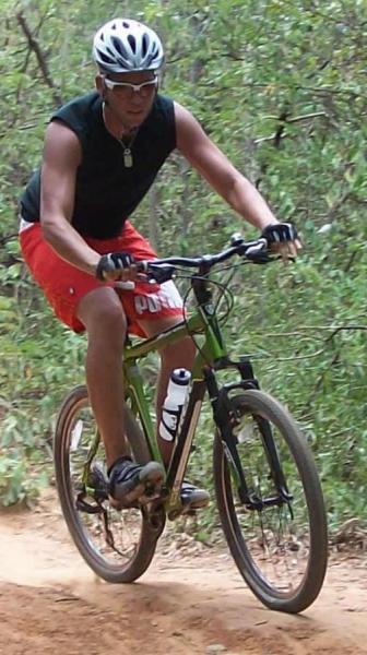 Trek 4300: A person riding a mountain bike along a dirt trail, surrounded by greenery. The cyclist is wearing a helmet, a sleeveless black shirt, and red shorts. They are in an active riding posture, focused on the trail ahead.