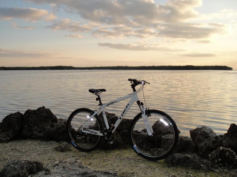 Trek 4500: A white mountain bike parked on rocky shorelines by a calm body of water, with a sunset sky in the background.