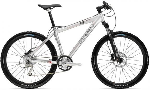 Trek 6500: A silver Trek mountain bike featuring a lightweight frame, front suspension fork, and disc brakes. The bike has black tires with blue accents and a comfortable saddle. It is positioned at an angle, showcasing its design.
