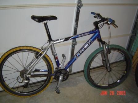 Trek 8000: A blue and silver Trek mountain bike with yellow and green tires, leaning against a garage wall. The bike features a front suspension and has a black saddle. The image is dated January 28, 2005.
