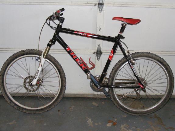 Trek 820: A black Trek mountain bike with red accents, showing dirt on the tires, parked in front of a garage door.