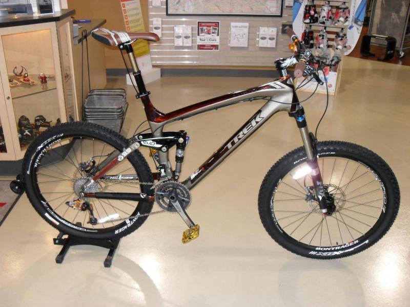 Trek Remedy 9.9: Alt tag: "A Trek mountain bike displayed in a shop, featuring a sleek design with a silver and reddish frame, wide tires, and a visible drivetrain, resting on a display stand."