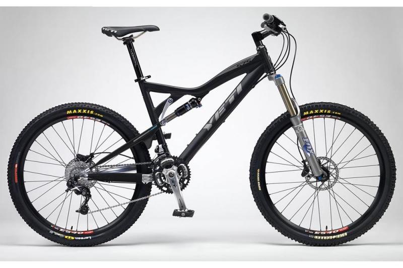Yeti 575: A black mountain bike with sleek design, featuring a lightweight frame and high-quality components. The bike is equipped with front suspension forks, wide tires with tread patterns designed for traction, and disc brakes. The branding logo is prominently displayed on the frame. The background is a simple gradient, emphasizing the bike's features.