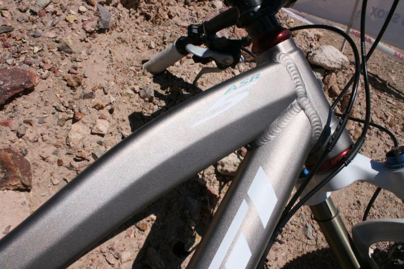 Yeti ASR 5 Alloy: Close-up view of a mountain bike frame with a metallic finish, showcasing the frame's design and components against a rocky terrain background.