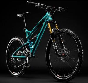 Yeti SB66: A modern mountain bike with a turquoise frame and gold suspension forks, positioned at an angle against a black background, highlighting its sleek design and rugged tires.