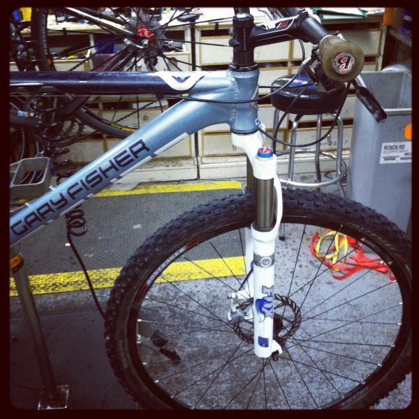 Gary Fisher Paragon: Alt tag: "Close-up view of a gray Gary Fisher mountain bike, showcasing the front wheel, suspension fork, and handlebars in a workshop setting."