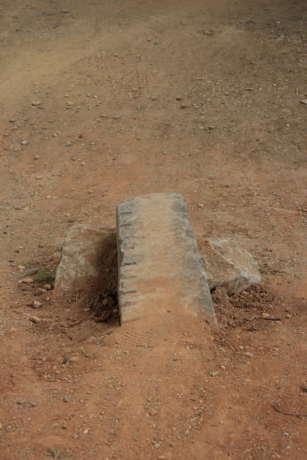 A weathered concrete block sits on a dirt surface surrounded by small stones and gravel, with a faint path leading towards it. Belle Isle mountain bike trail.